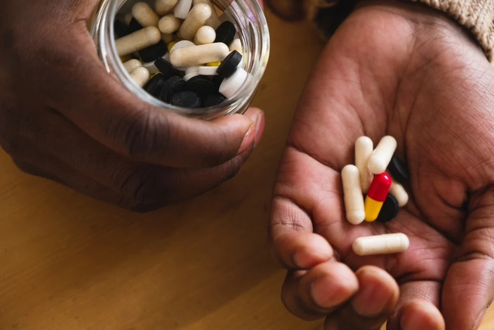 Close-up of the hands of an African man holding various capsules, portraying the daily routine of vitamin and medication consumption. Emphasizes health and wellness. Diverse Supplements in Hand