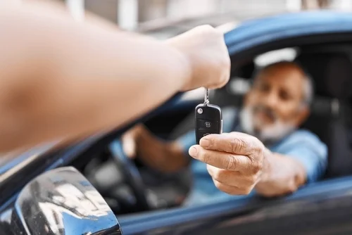 Senior grey-haired man holding key of new car at street