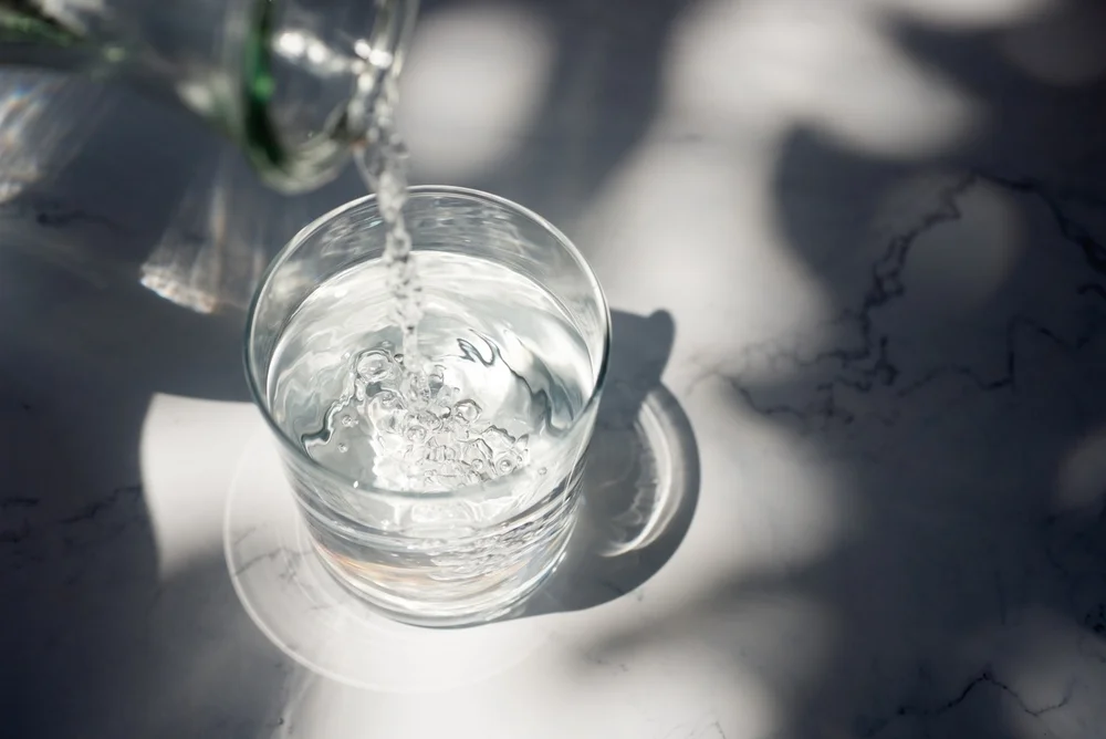 Pouring drinking water into glass on white marble table.