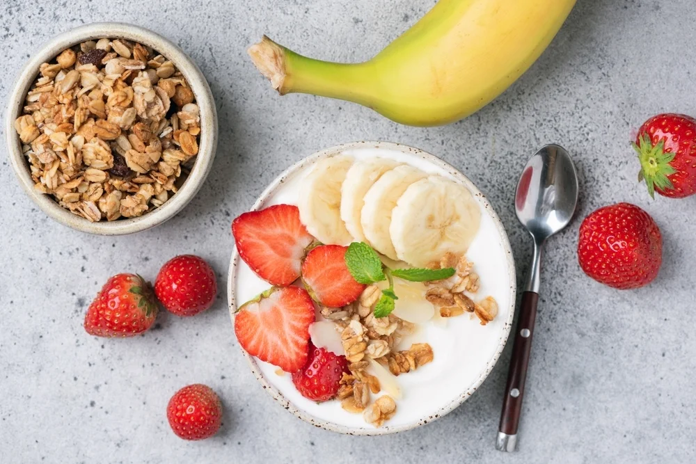 Healthy granola yogurt bowl with banana, strawberries and crunchy granola. Top view