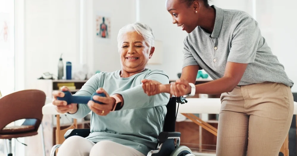 Wheelchair, woman and dumbbell for physical therapy, help and medical health. Clinic, weights and physiotherapy for happy senior person with disability in rehabilitation, exercise muscle or fitness