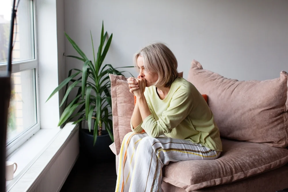 Sad Worried middle age woman sitting on Couch at home. Stress woman sitting thoughtfully alone on sofa