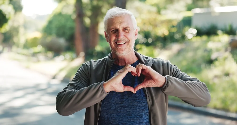 Park, heart hands and portrait of senior man for wellness, cardio health and fitness. Outdoor, retirement and happy elderly person with emoji for active hobby, exercise and walking for mobility