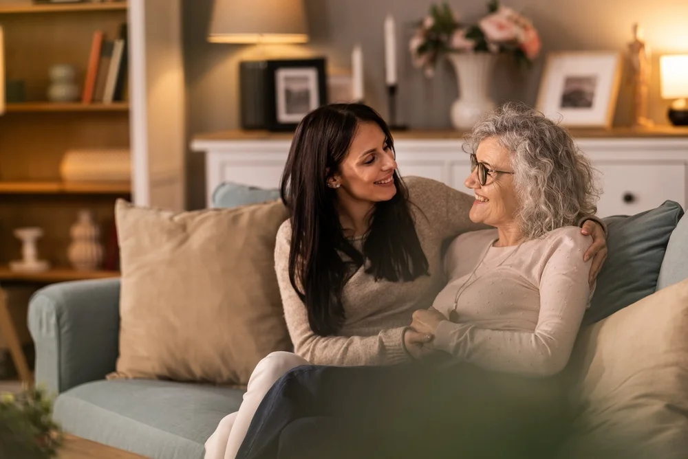 Adult daughter having conversation with her adult mother while they sitting on couch together in living room.