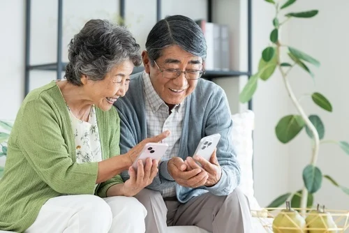 A senior Japanese couple looking at their smartphones in their living room.